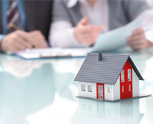 a close up of two people going over paperwork with a tiny model home in front of them